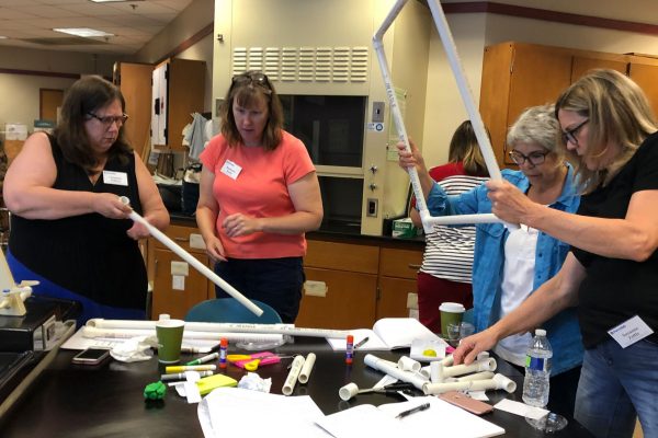 A photo of four teachers working with activity supplies, including PVC pipes and markers.