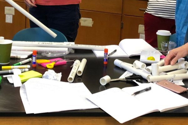 A photo of four teachers working with activity supplies, including PVC pipes and markers.