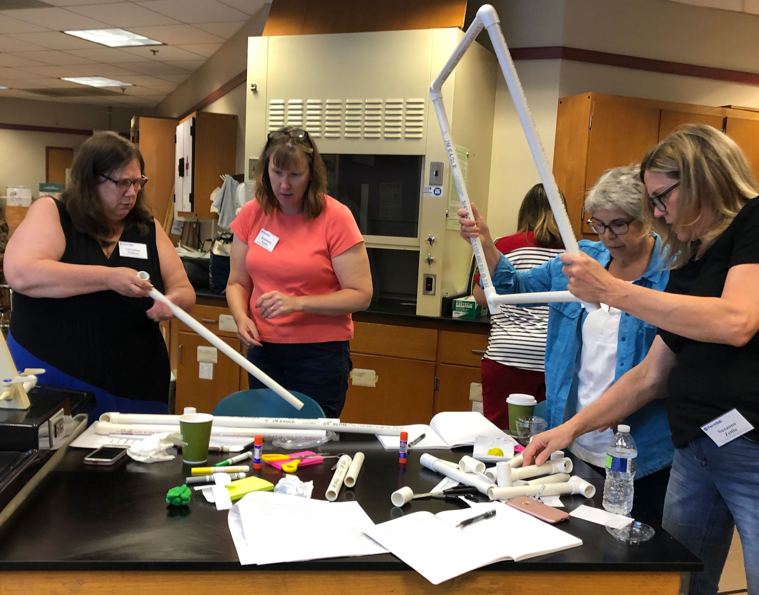 A photo of four teachers working with activity supplies, including PVC pipes and markers.