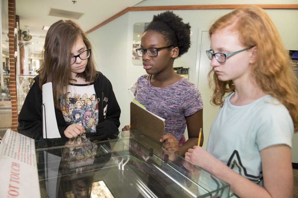 3 students looking into the cloud chamber exhibit in the Detectors Room. 