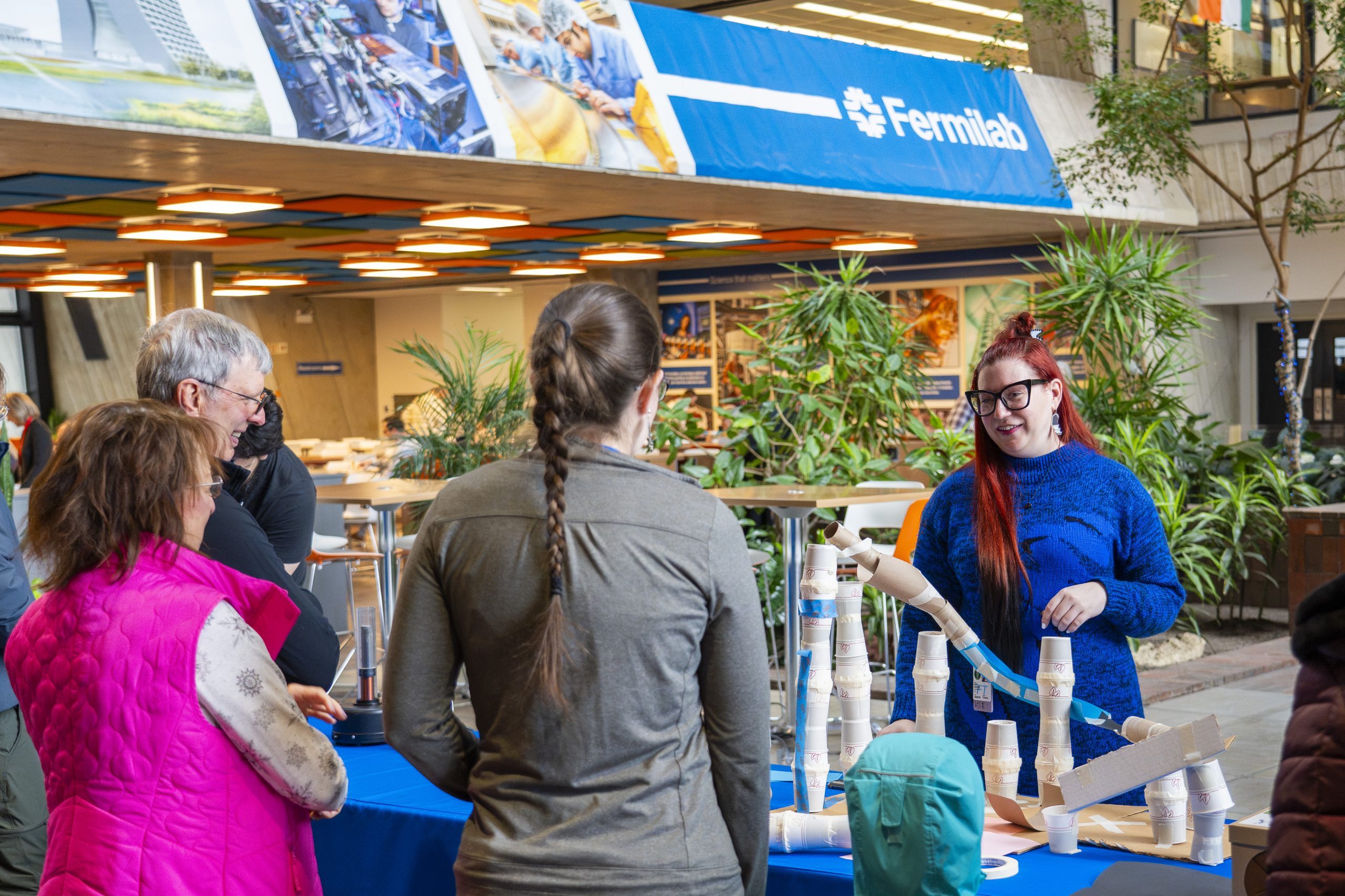 Several people in Wilson Hall smiling and talking. The table next to them is filles with activity supplies, such as tape and cardboard tubes.